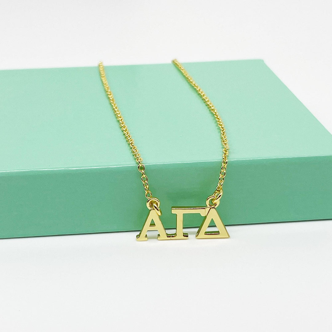 A gold-colored necklace with the letters "AIA" on it, resting on a green surface.