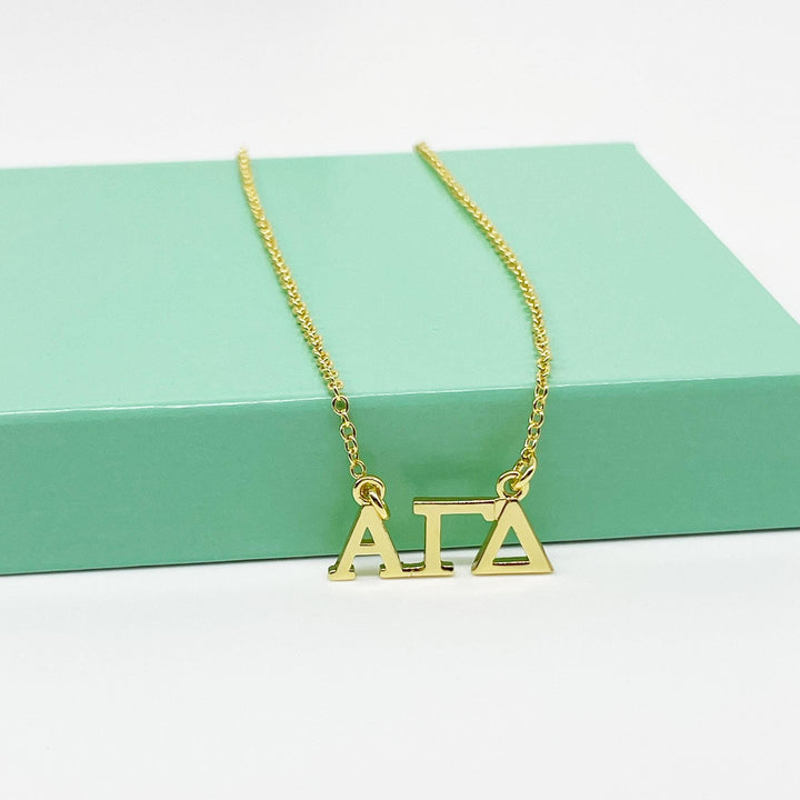 A gold-colored necklace with the letters "AIA" on it, resting on a green surface.