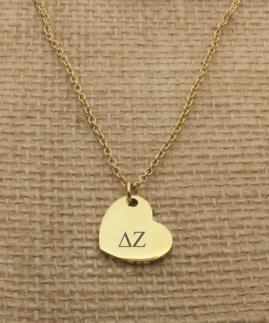 A gold-colored necklace with a heart-shaped charm featuring the letters "ΔΩ" engraved on it.