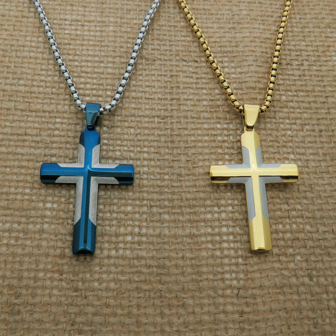Two cross-shaped pendants, one in blue and one in gold, are displayed on a woven surface.