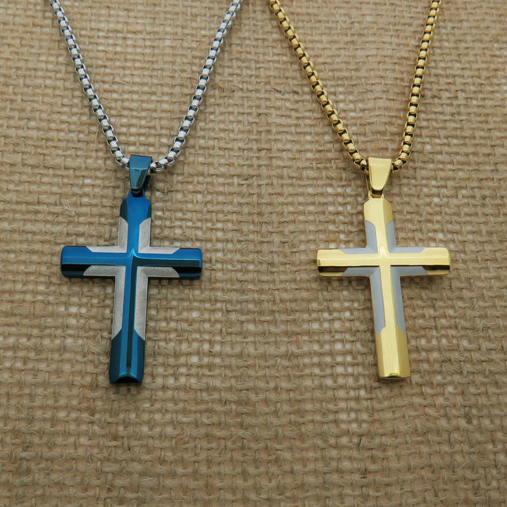 Two cross-shaped pendants, one in blue and one in gold, are displayed on a woven surface.