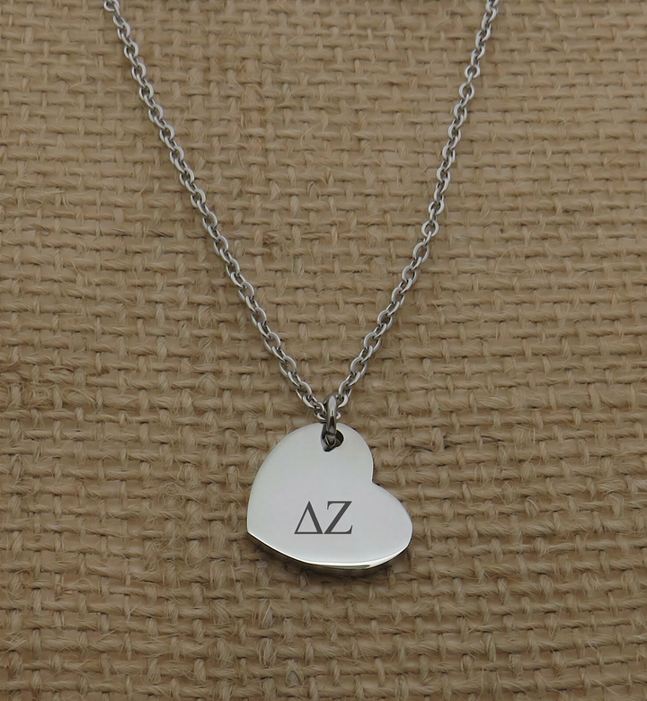 A silver heart-shaped charm necklace with the letters 'ΑΛ' engraved on it.