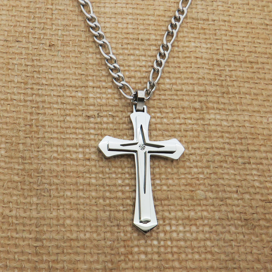 A silver cross pendant necklace is displayed against a woven fabric background.