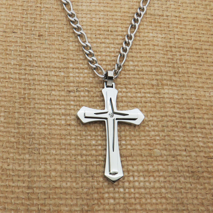 A silver cross pendant necklace is displayed against a woven fabric background.