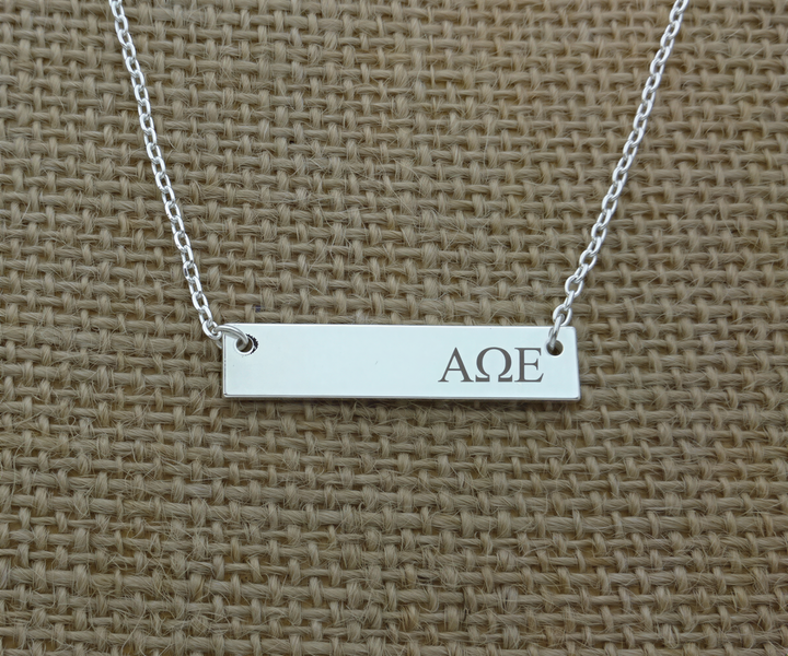 A silver necklace with a rectangular pendant engraved with the letters "AΔE".