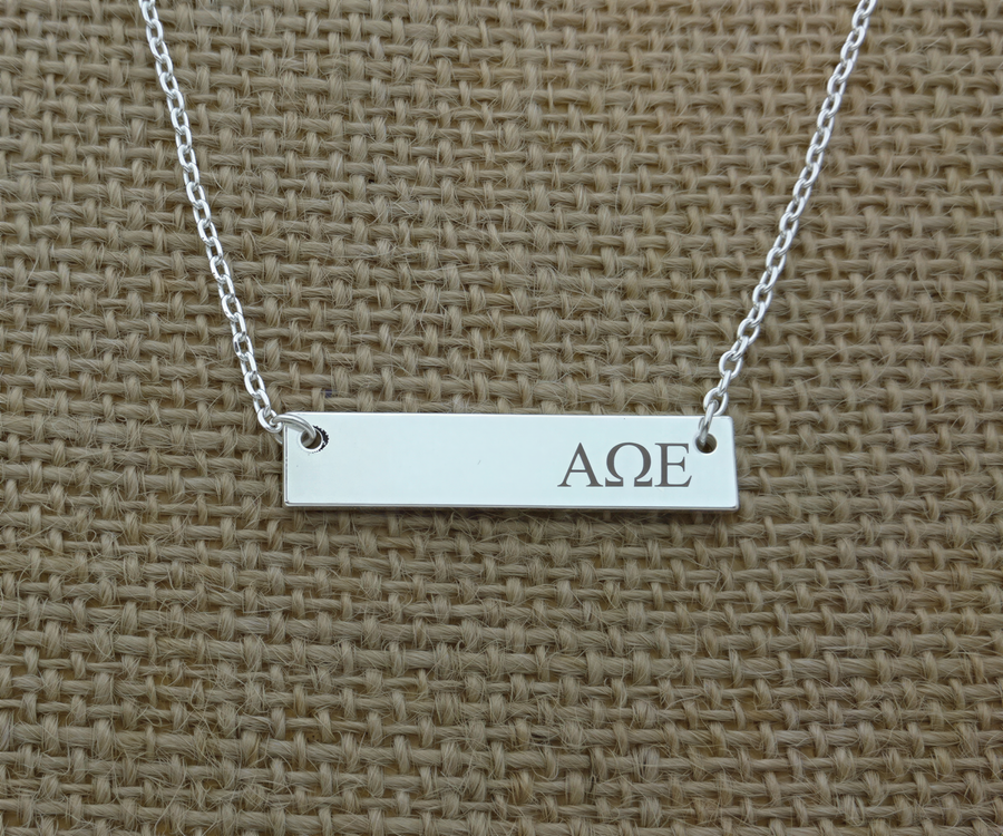 A silver necklace with a rectangular pendant engraved with the letters "AΔE".