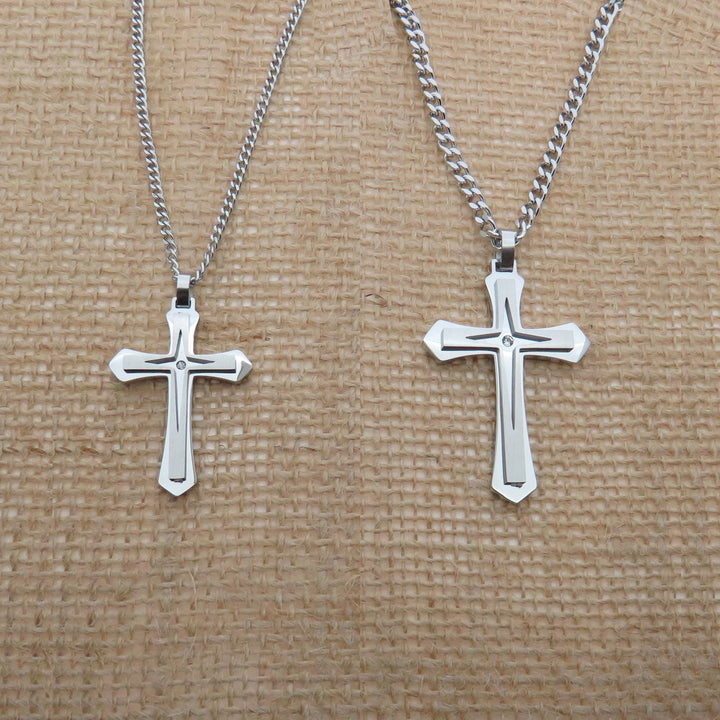 Two silver cross necklaces with a beige background.