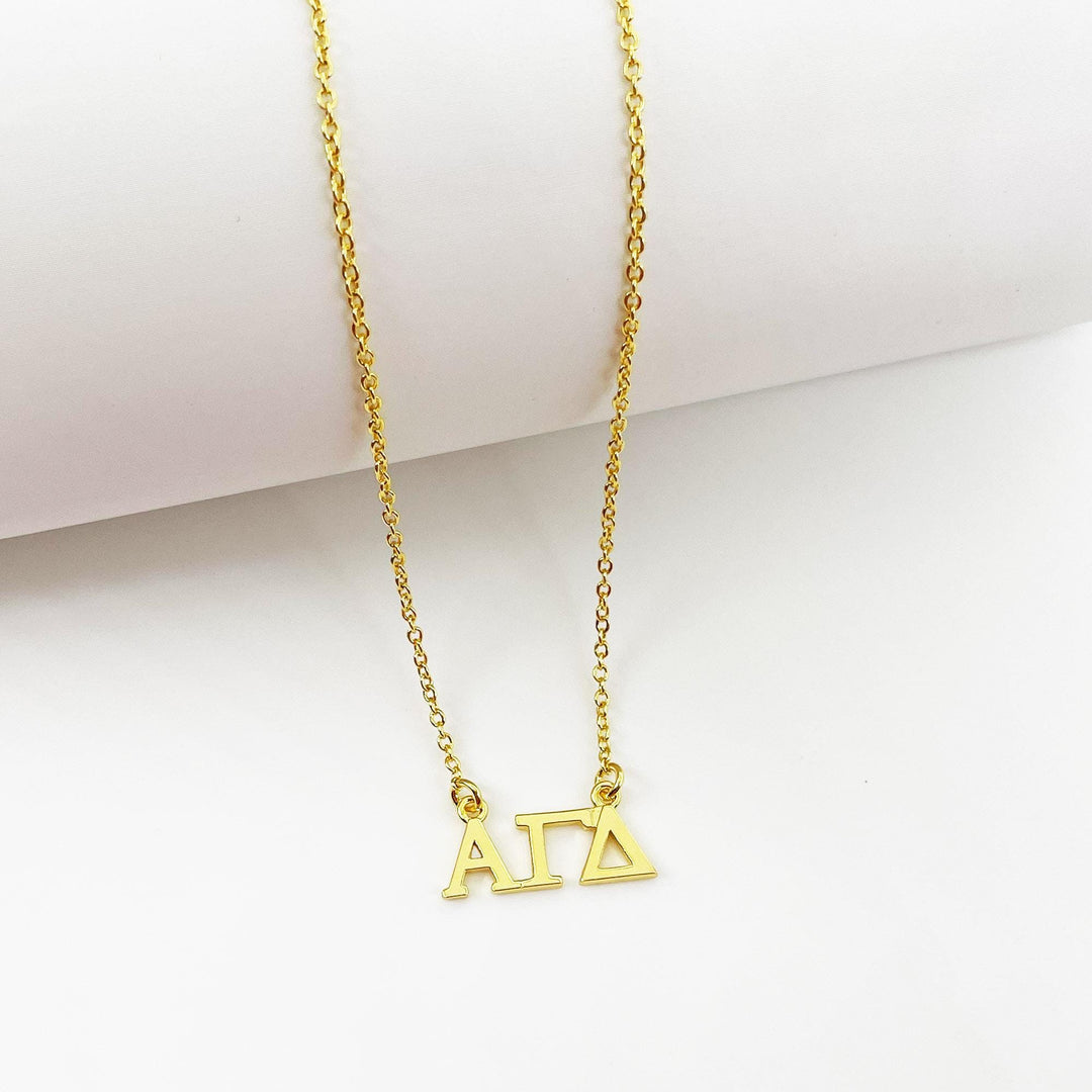 A gold-colored necklace with the letters 'ΑΓΑΙ' (ΑΓΑΙ) engraved on it.