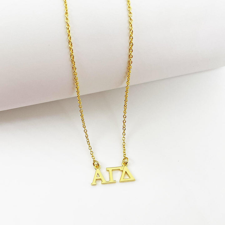 A gold-colored necklace with the letters 'ΑΓΑΙ' (ΑΓΑΙ) engraved on it.