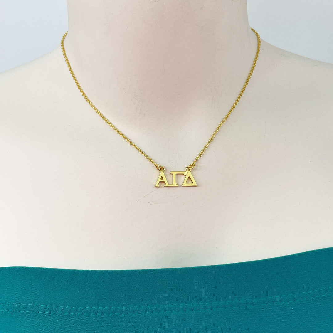A gold-colored necklace with the letters 'ΑΓΑΙ' (ΑΓΑΙ) pendant hanging from it.