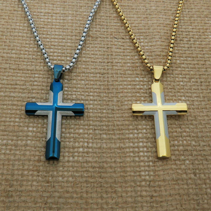 Two cross-shaped pendants, one in blue and one in gold, are displayed on a woven surface.