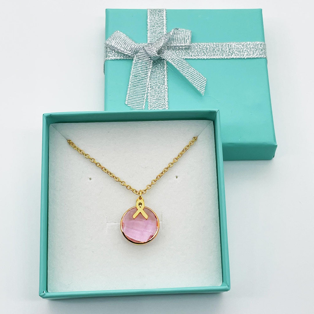 A necklace with a pink gemstone pendant is displayed in a turquoise jewelry box with a silver bow.