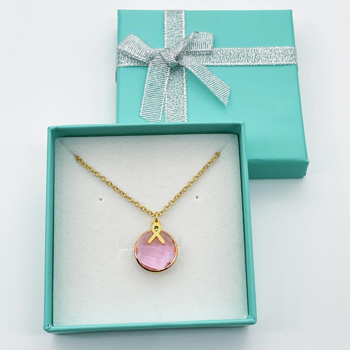 A necklace with a pink gemstone pendant is displayed in a turquoise jewelry box with a silver bow.