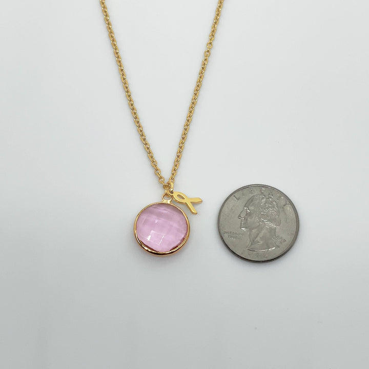 A gold necklace with a round pink gemstone is shown next to a United States quarter coin.