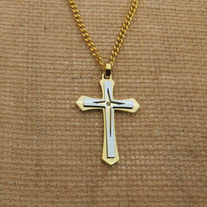A gold cross pendant with a diamond in the center, hanging from a chain against a textured beige background.