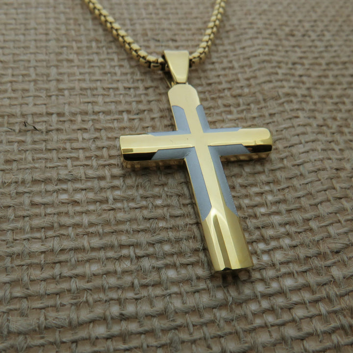 A gold-colored cross pendant with a blue and gold design is displayed on a woven fabric surface.
