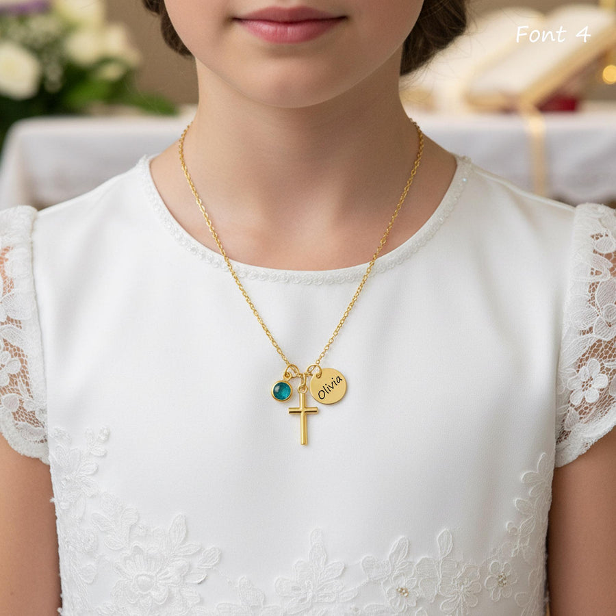 A close-up of a person wearing a gold cross necklace with a small charm and the name "Olivia" engraved on it.