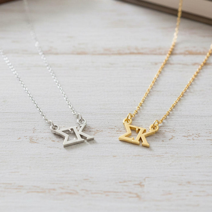 Two necklaces with the letters 'X' and 'K' on them, one silver and one gold, are displayed on a wooden surface.
