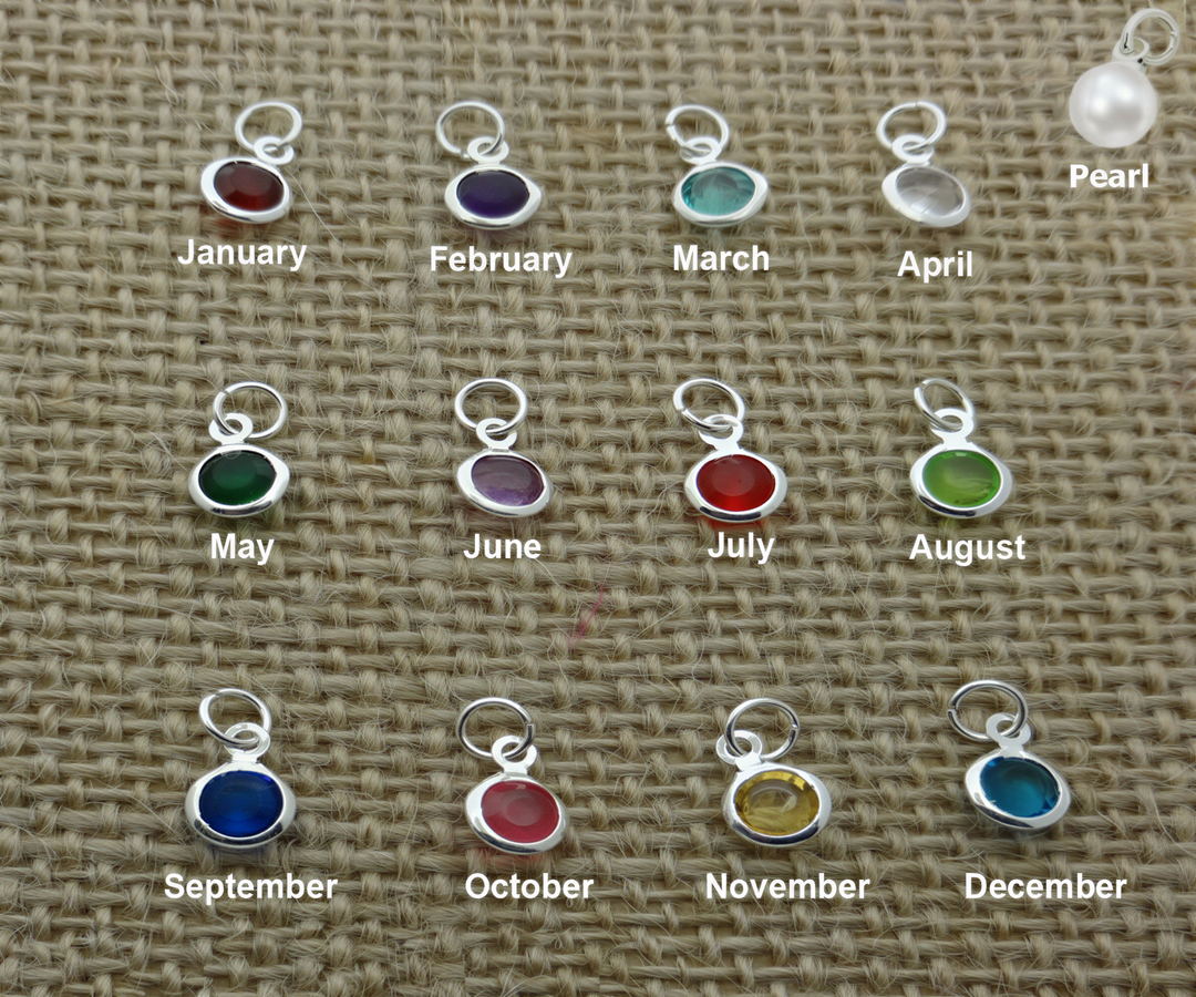 a collection of twelve silver charms, each representing a different month of the year, arranged on a woven surface.