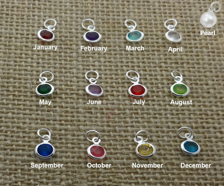 a collection of twelve silver charms, each representing a different month of the year, arranged on a woven surface.