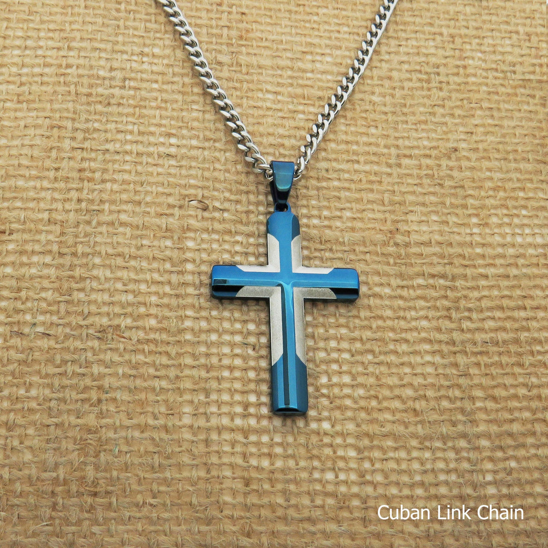 A blue and white cross pendant necklace with a silver chain is displayed on a woven fabric background.