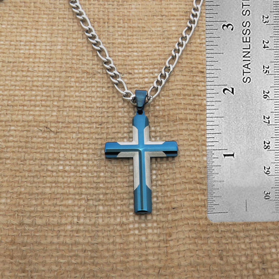 A blue and white cross pendant is displayed on a chain, with a ruler placed next to it to provide a size reference.