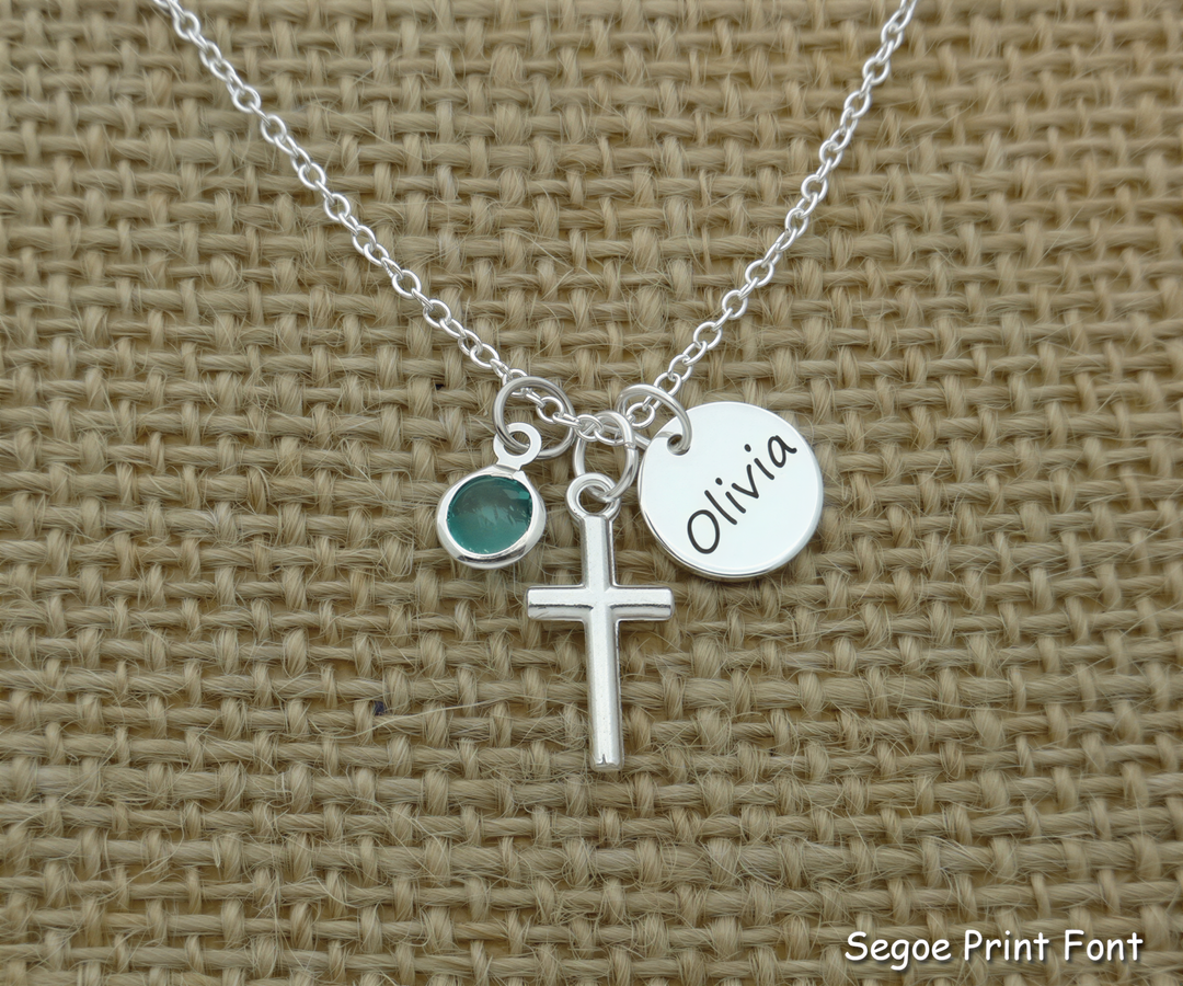 A silver cross necklace with a charm and a name tag attached to it.