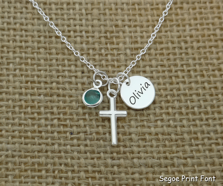 A silver cross necklace with a charm and a name tag attached to it.