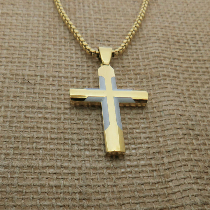 A gold-colored cross pendant necklace is displayed on a woven fabric surface.
