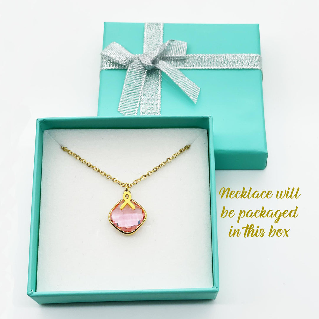 A necklace with a pink gemstone is displayed in a turquoise jewelry box with a silver ribbon bow.