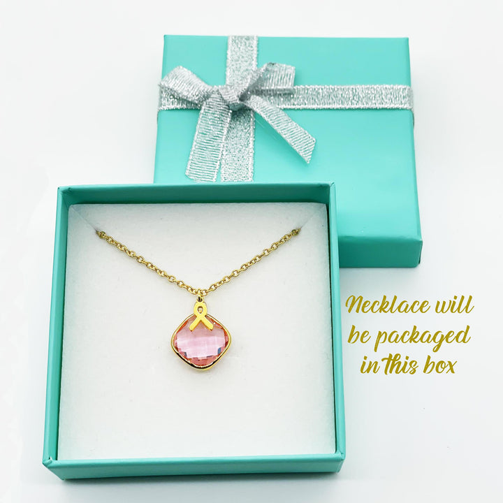 A necklace with a pink gemstone is displayed in a turquoise jewelry box with a silver ribbon bow.