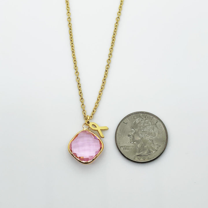 A gold necklace with a pink gemstone pendant is shown next to a United States quarter coin.
