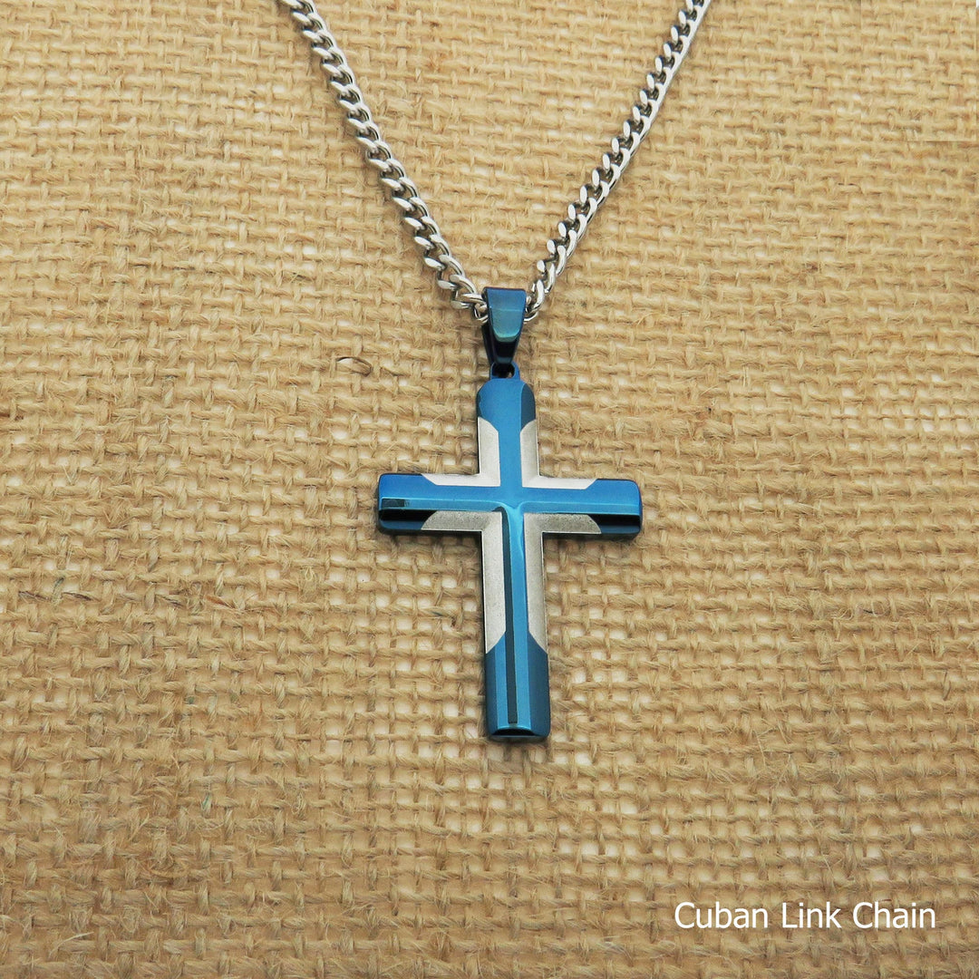 A blue and white cross pendant necklace with a silver chain is displayed on a woven surface.