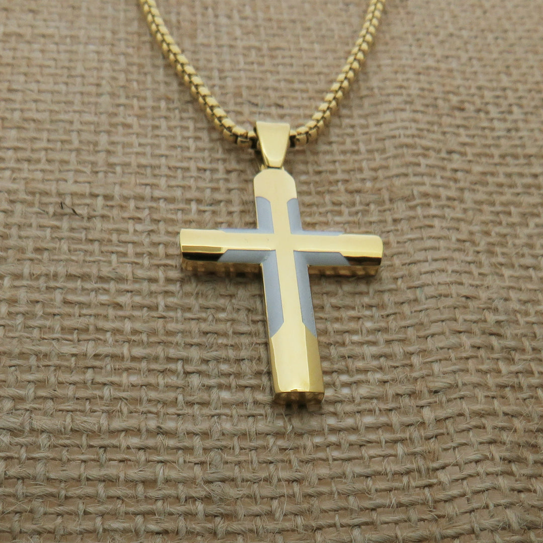 A gold-colored cross pendant necklace is displayed on a woven fabric surface.