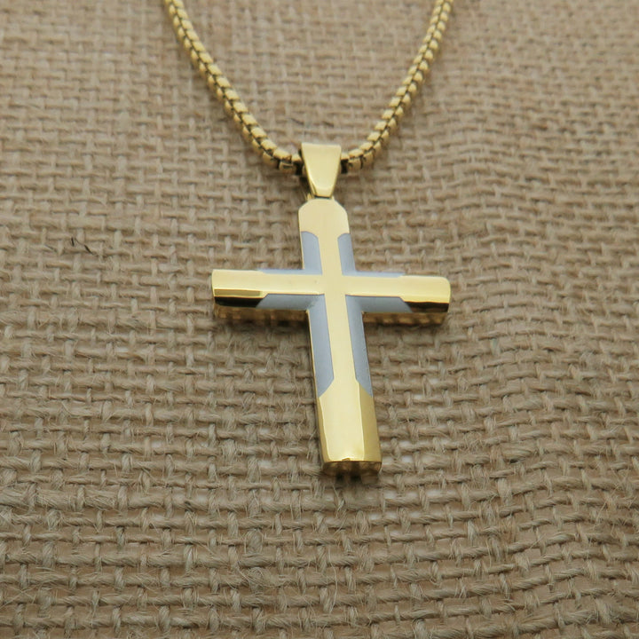 A gold-colored cross pendant necklace is displayed on a woven fabric surface.
