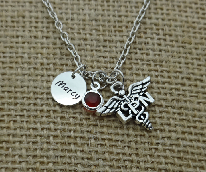 A silver necklace with a charm pendant, featuring a medical symbol and the name "Marcia" engraved on a round metal tag.