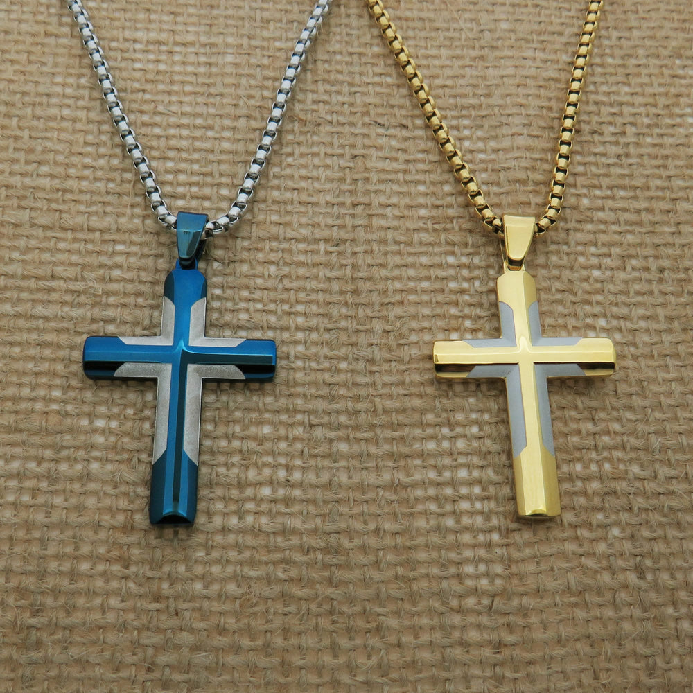 Two cross-shaped pendants, one in blue and one in gold, are displayed on a woven surface.