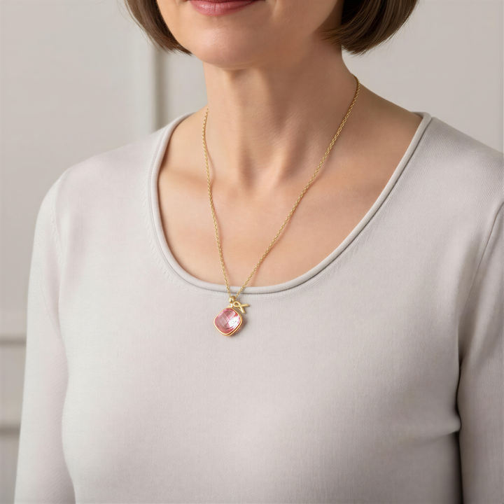 A woman wearing a gold necklace with a pink pendant is shown in the image.