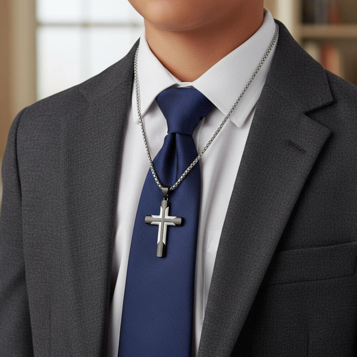 A man wearing a gray suit jacket, white shirt, and blue tie with a silver cross pendant.