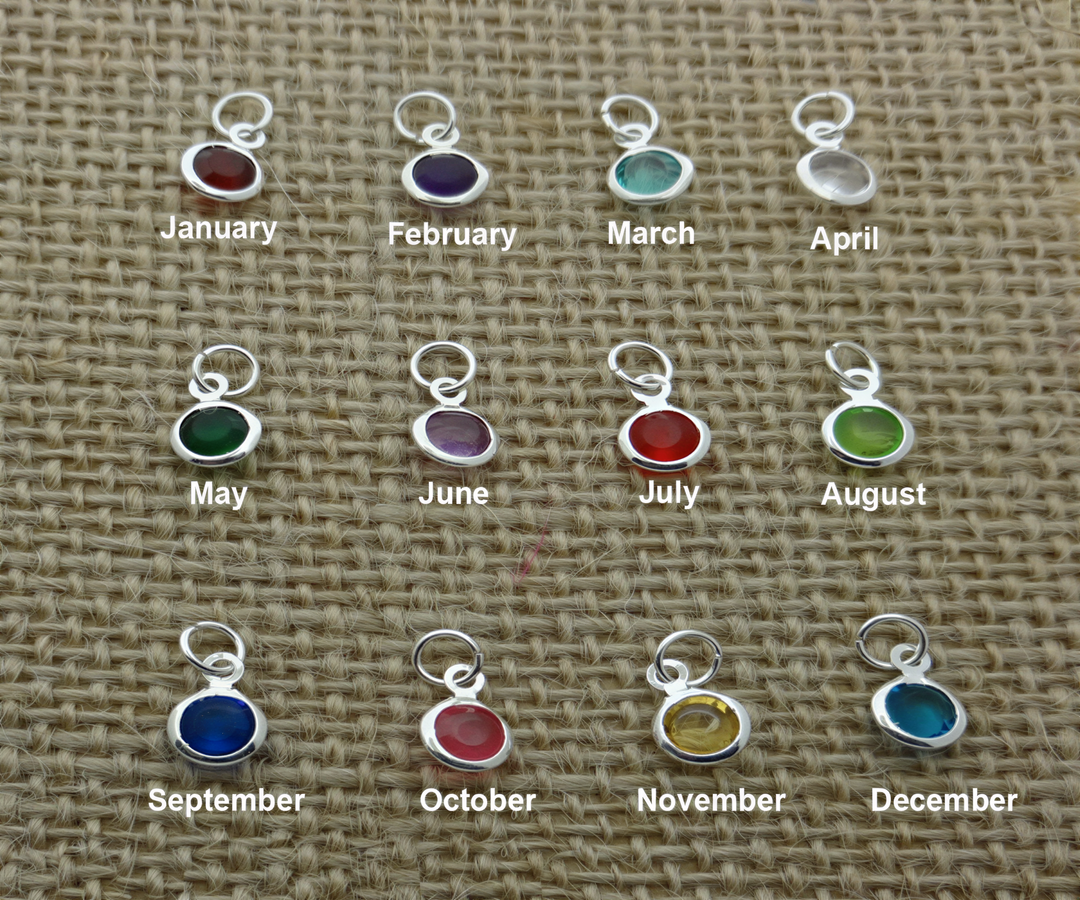 a collection of twelve silver charms, each representing a different month of the year, arranged in a grid pattern on a woven surface.