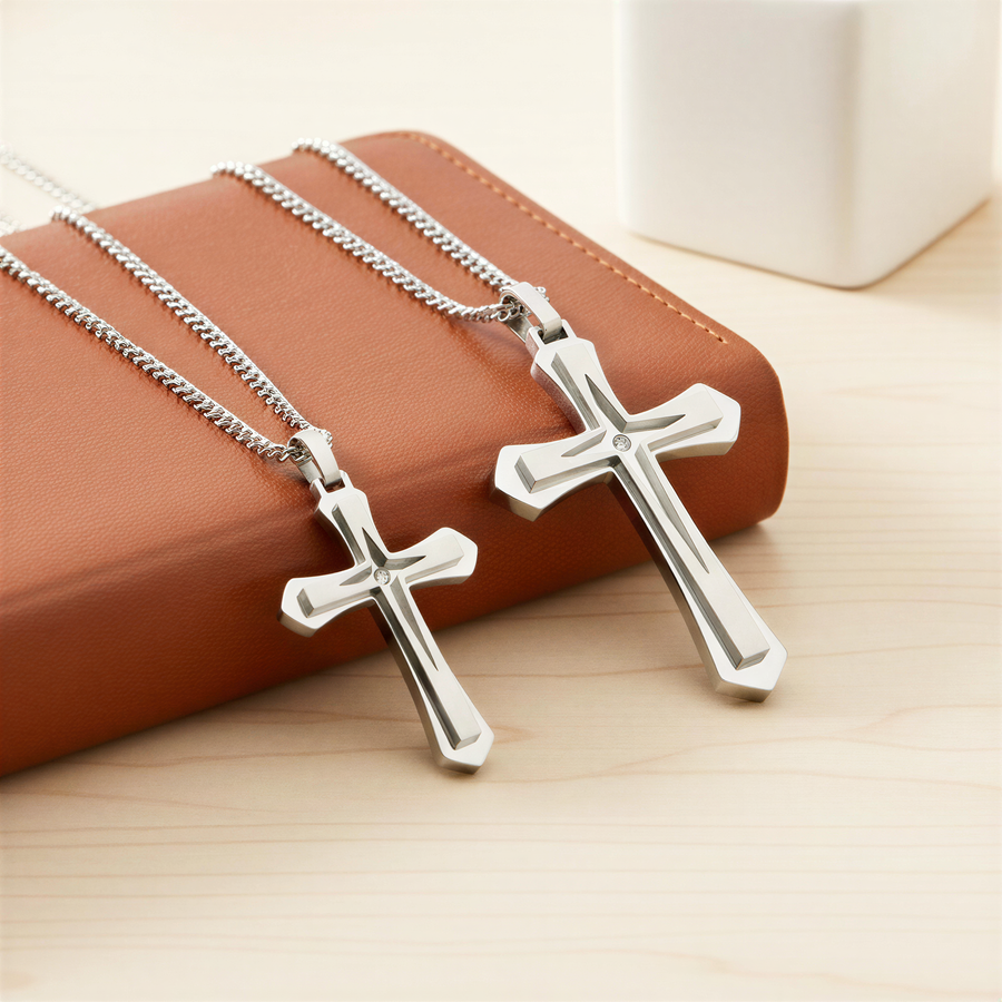 Two silver cross necklaces with different sizes are displayed on a brown leather surface, with a white object in the background.