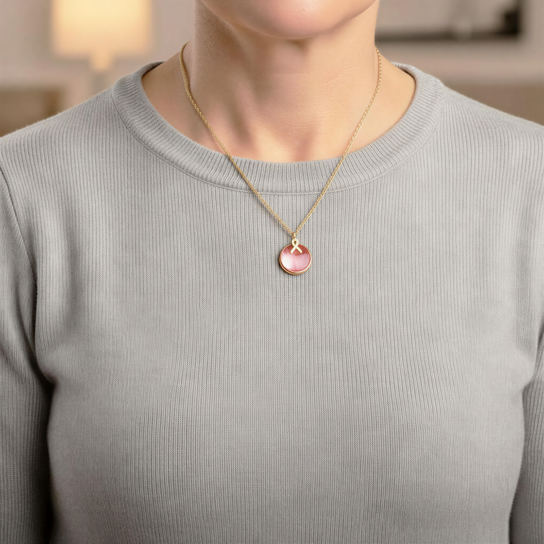 A woman wearing a gray sweater and a gold necklace with a pink pendant.