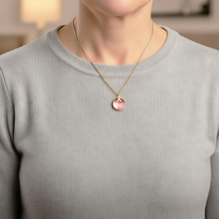 A woman wearing a gray sweater and a gold necklace with a pink pendant.
