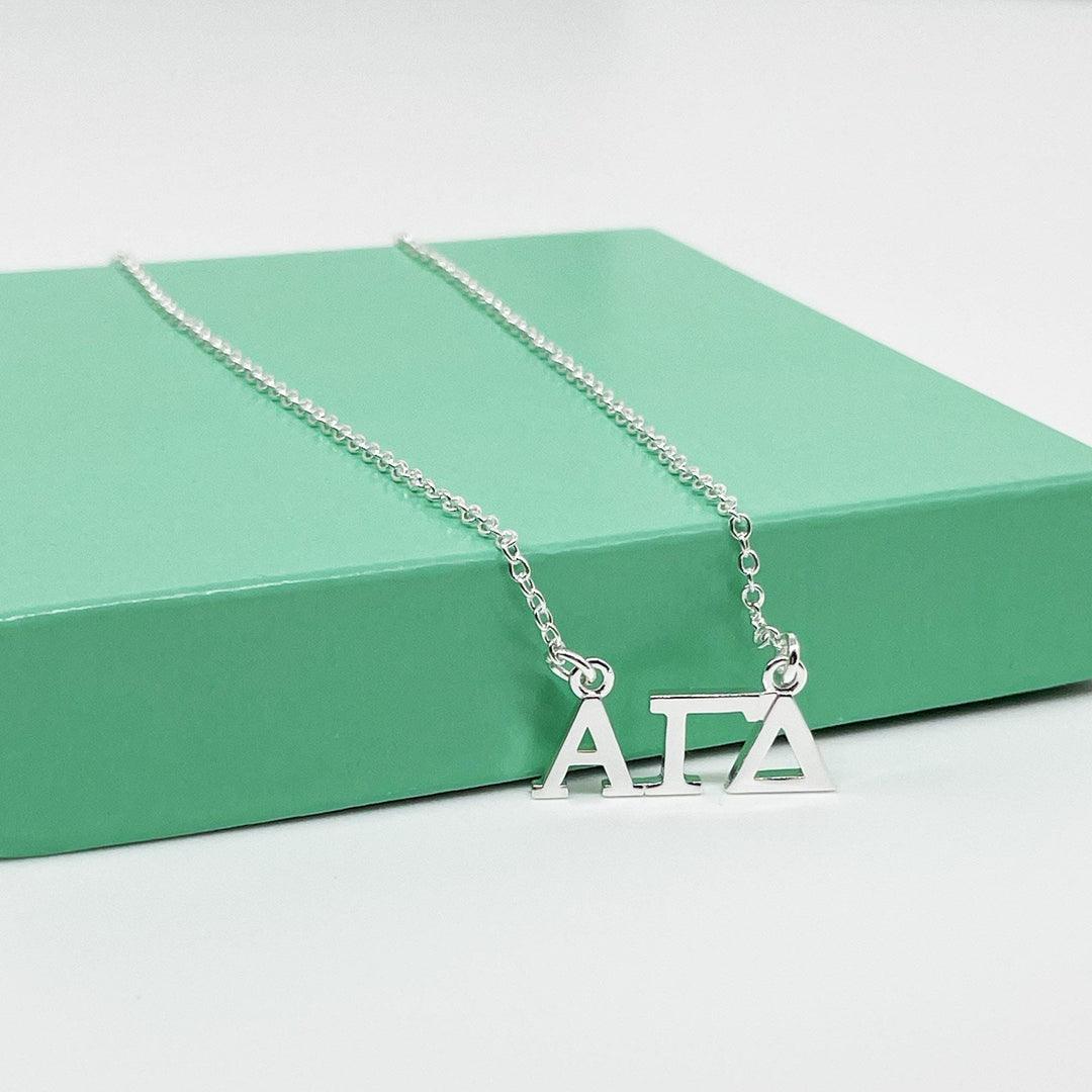 A silver necklace with the letters "A" and "T" on it, resting on a green surface.