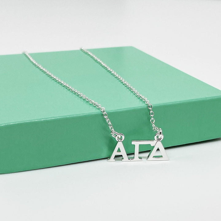 A silver necklace with the letters "A" and "T" on it, resting on a green surface.